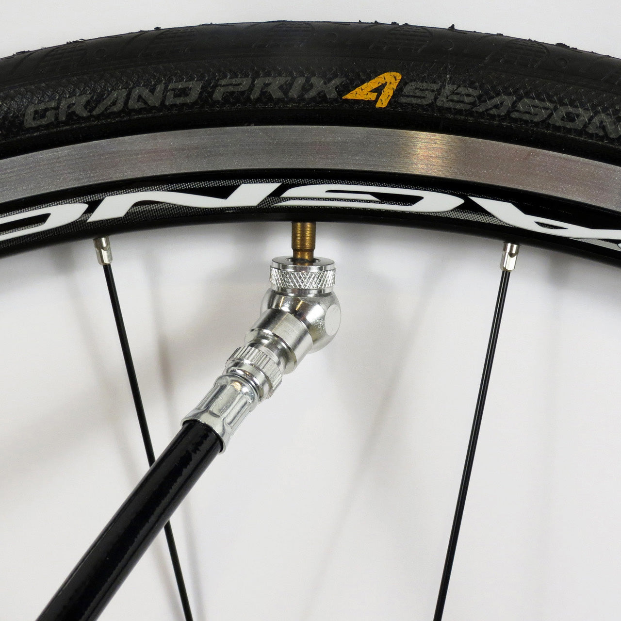 A black pump with the Prestacycle Angle Mini Presta Head attached to a Continental Grand Prix 4 Season tubeless tire, mounted on a black and silver rim.