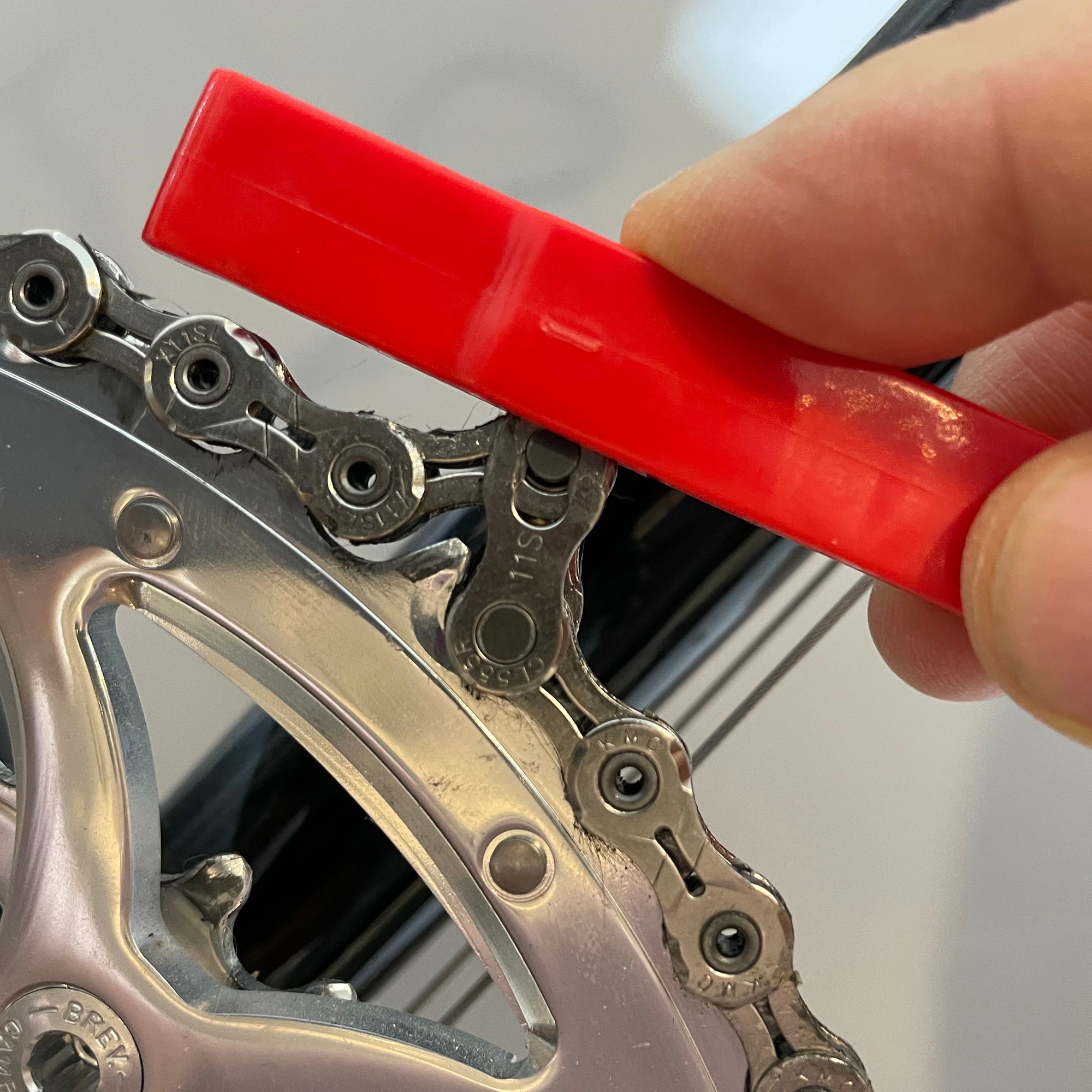 A hand uses the Prestacycle Prestalever GO 5-in-1 Multi-tool Tire Lever near a bicycles gears, possibly to check chain alignment or wear.