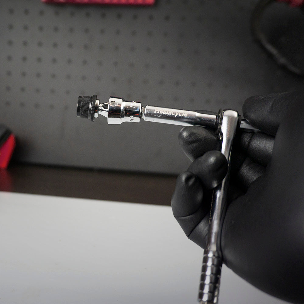 A gloved hand holds the Prestacycle Bits Swivel QR Torque Wrench Adapter by Prestacycle—an essential tool for use with torque wrenches—against a black pegboard backdrop.