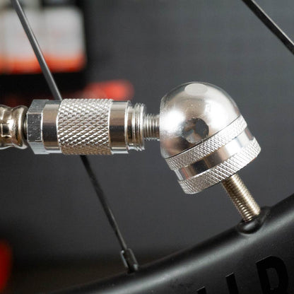 Close-up of a Prestacycle Prestaflator Bicycle Tire Inflator nozzle on a Presta valve with black spokes in the background—perfect for inflating tubeless tires using this Presta &amp; Schrader air compressor tool.