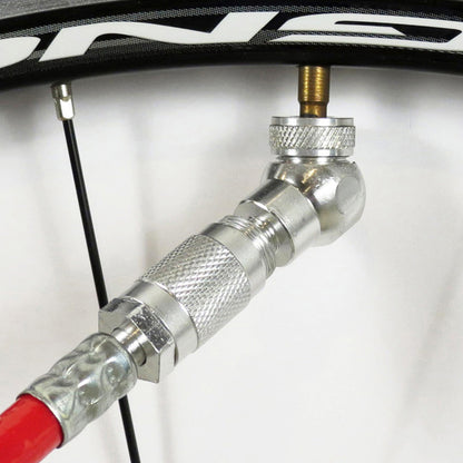 A close-up of the Prestacycle Angle Mini Presta Head with a metal adapter attached to a red pump hose, connected for inflation. The bike rim and spokes appear in the background—ideal for tubeless tire setups.