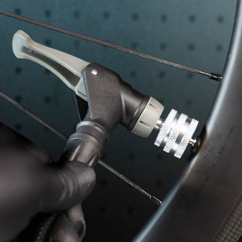 A gloved hand inflates a tubeless tire with a pump fitted with the Prestacycle Big Presta Head by Prestacycle.