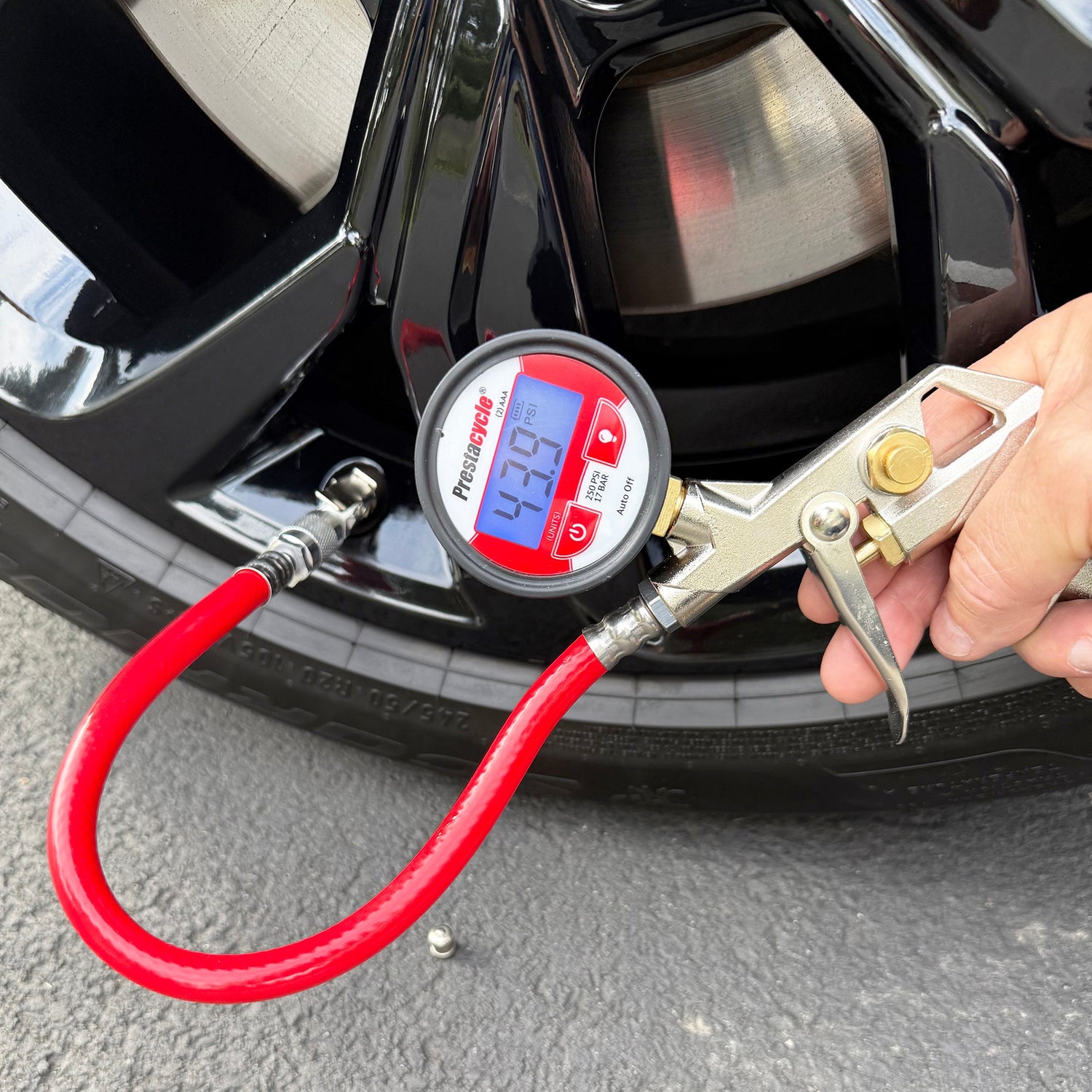 A close-up shows a Prestacycle Prestaflator Digital Bicycle Tire Inflator with red hose attached to a car tire valve, displaying 47.9 PSI, while a person presses the lever—compatible with Presta and Schrader valves and tubeless-safe.