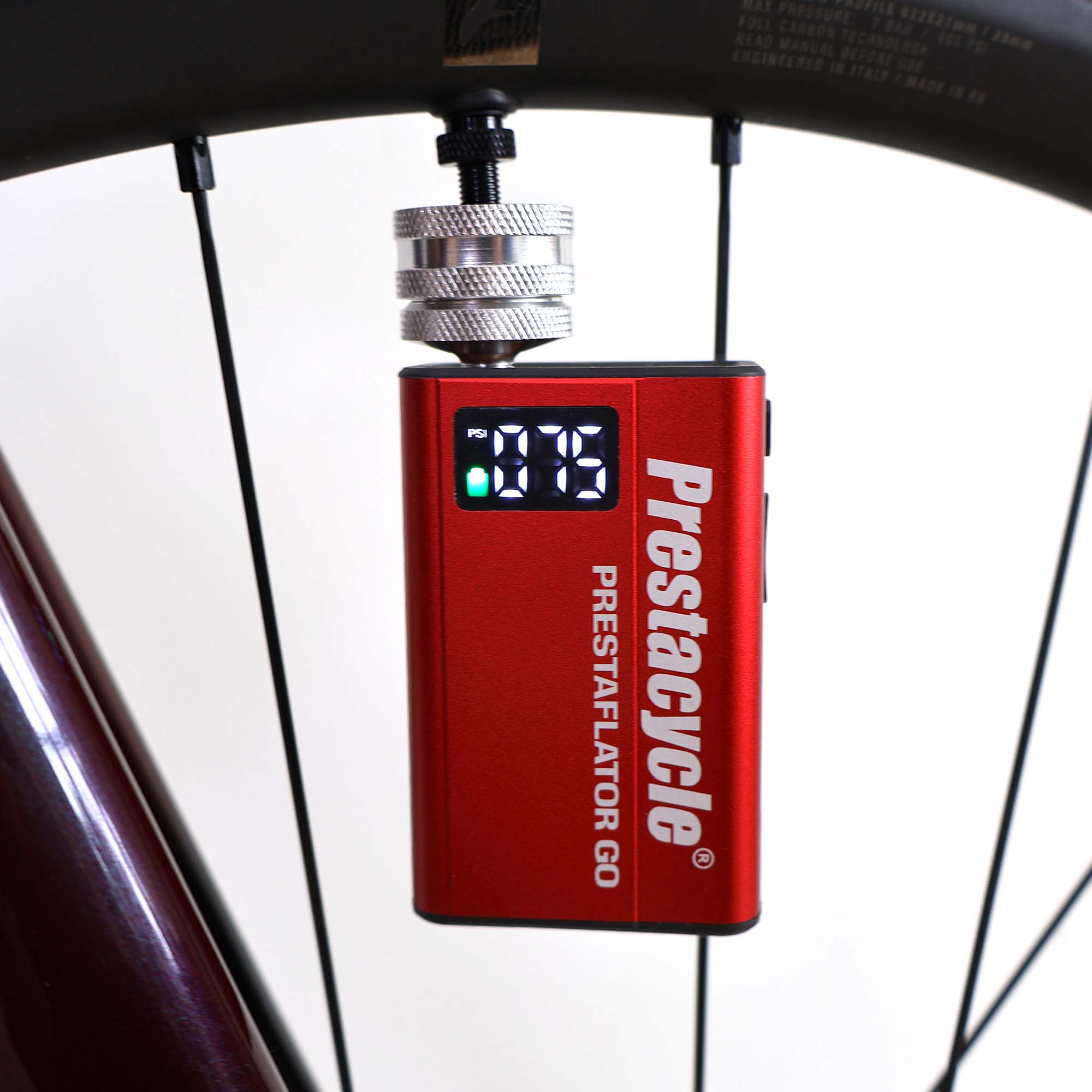 A Prestacycle Prestaflator GO Portable Digital Rechargeable Preset Bicycle Tire Inflator is attached to a bicycle tire valve, showing a digital screen reading of 19 psi.