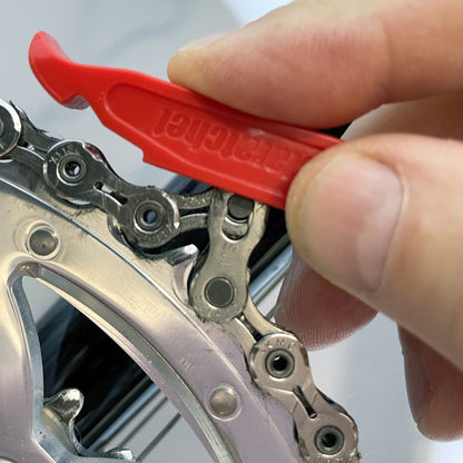 A hand uses the Prestacycle Prestaratchet GO Multi-tool Kit to check the wear on a silver bicycle chain fitted onto a metal gear.