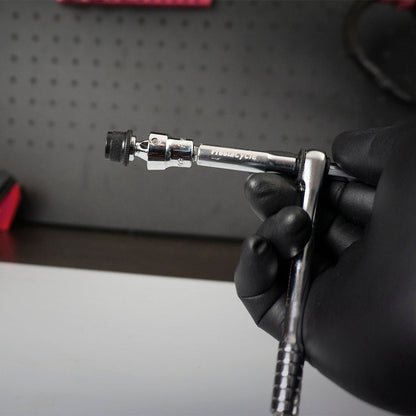 A gloved hand holds the Prestacycle Bits Swivel QR Torque Wrench Adapter by Prestacycle—an essential tool for use with torque wrenches—against a black pegboard backdrop.