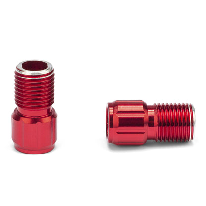 Two small red Prestacycle Prestadapter fittings for converting Schrader to Presta valves are shown on a white background. One stands upright showing its inner thread; the other lies on its side displaying external threading.
