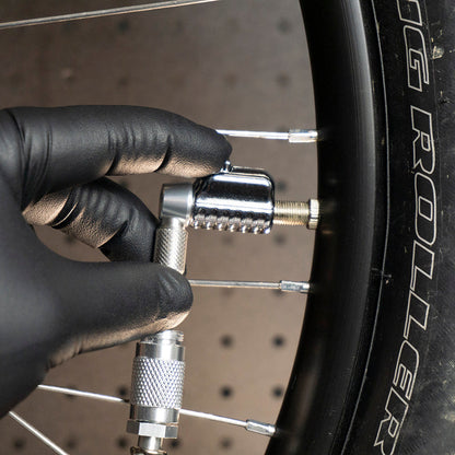 A gloved hand attaches a Prestacycle Pro Schrader Head by Prestacycle with an auto-lock mechanism to a bicycle tire valve; the sidewall shows the words BIG ROLLER.