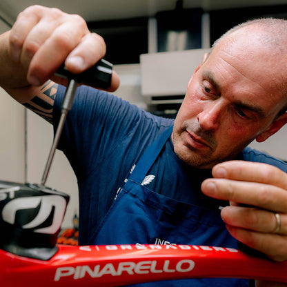A man in a blue apron focuses as he uses the Prestacycle Pro TorqKeys 4Nm T-Handle Torque-Limiting Bits Tool to adjust the handlebars of a red Pinarello bicycle indoors.