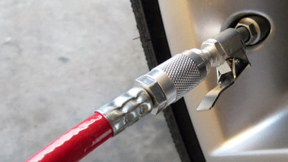 A close-up of the Prestacycle Prestaflator Digital Bicycle Tire Inflator, attached to a tire valve, quickly inflating the tire. The red hose and part of the rim are visible against the concrete floor in the background.